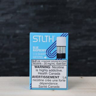 STLTH e cigarette Blue Raspberry nicsalt vape pods blue box in focus with health canada warming nicotine is highly addictive on a table inside Twisted Sisters Vape Shop near me